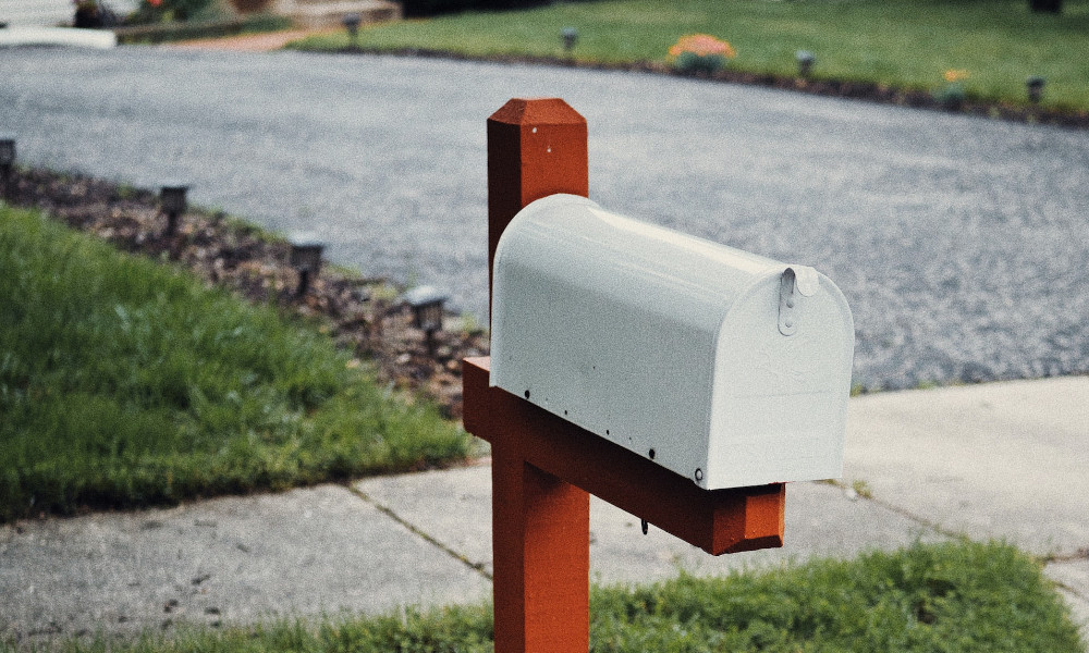 An image of a white mailbox with a red post.